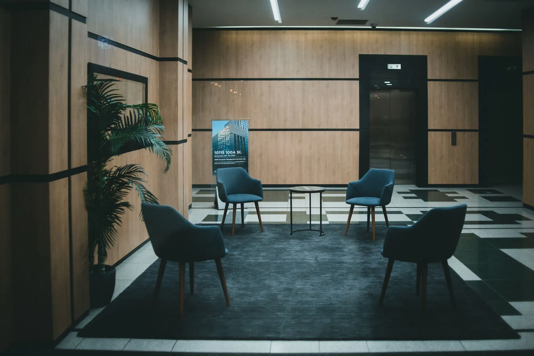 A calm lounge with dark green chairs and tall plants